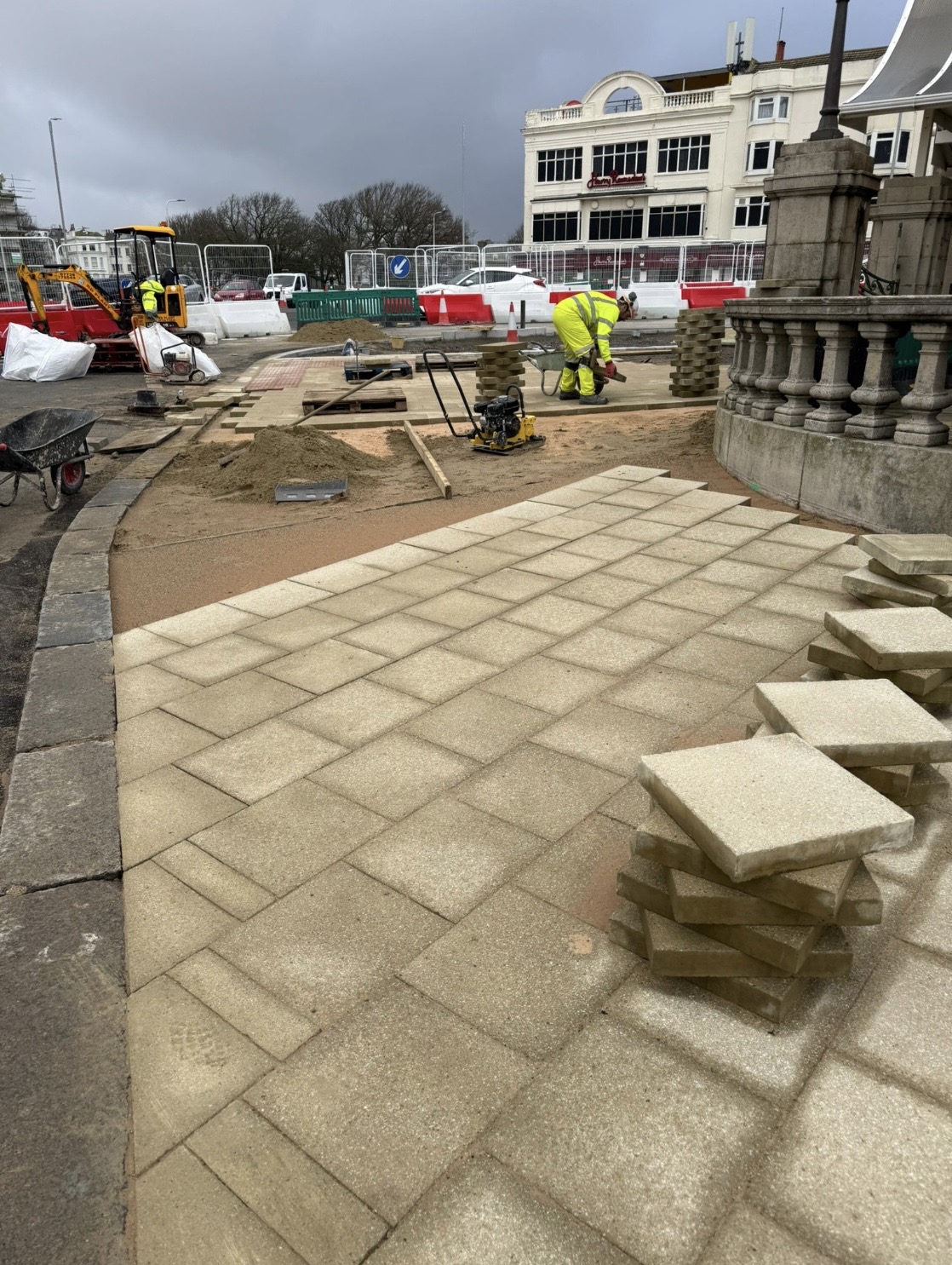 Paving works in progress with operative laying buff slabs near stone monument