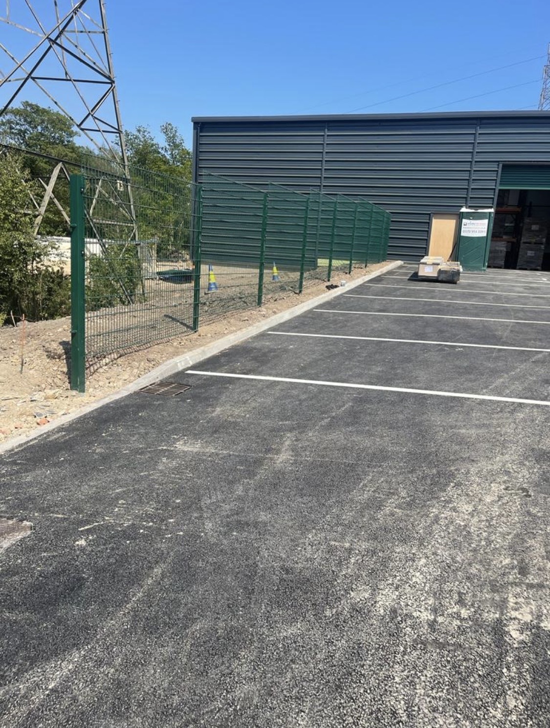New asphalt parking bays and green security fencing beside an industrial unit