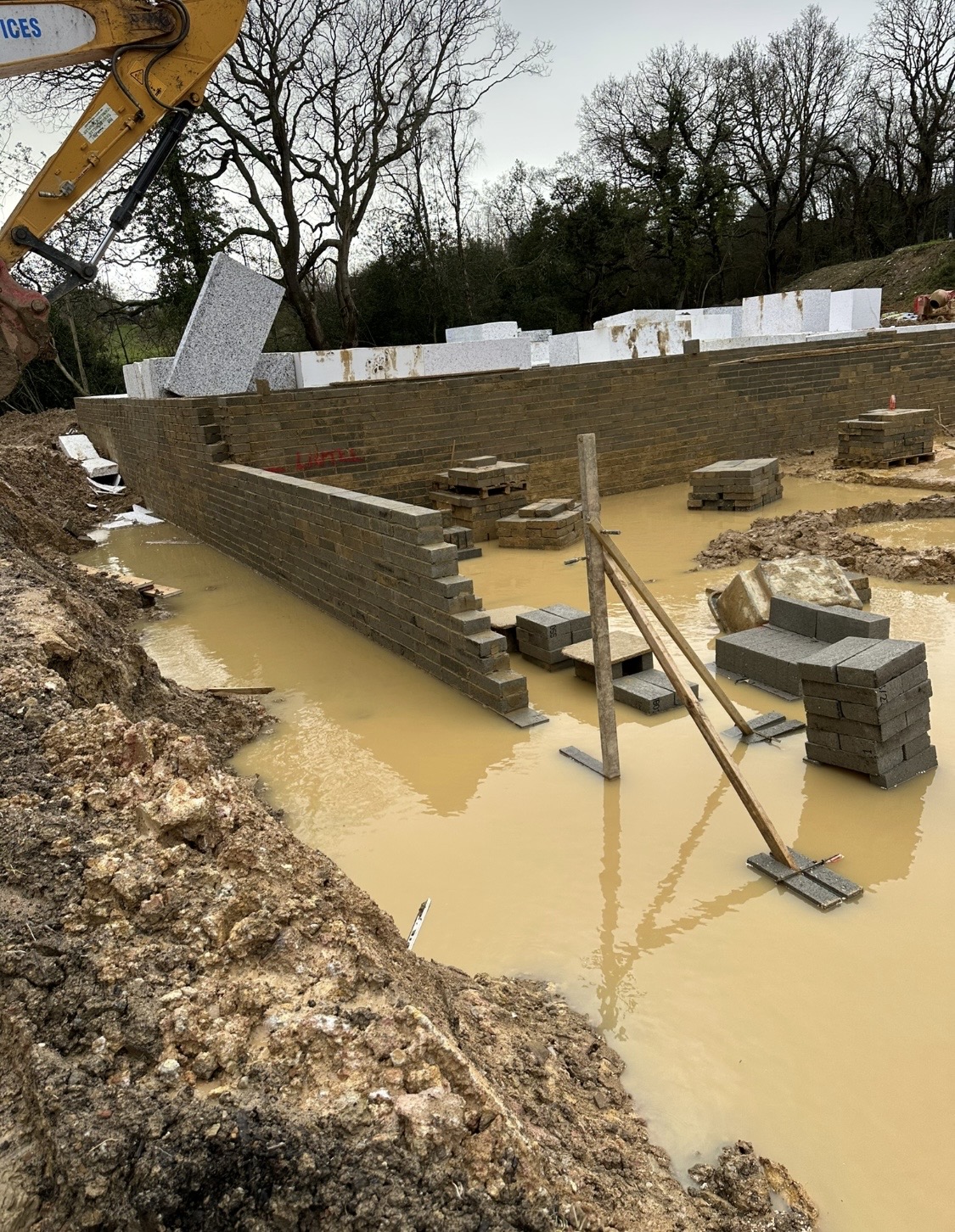 Buff brick retaining wall with stacked materials on a wet site
